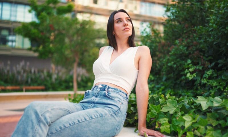 devojka u svetlim farmerkama i belom topu sedi i fotografiše se