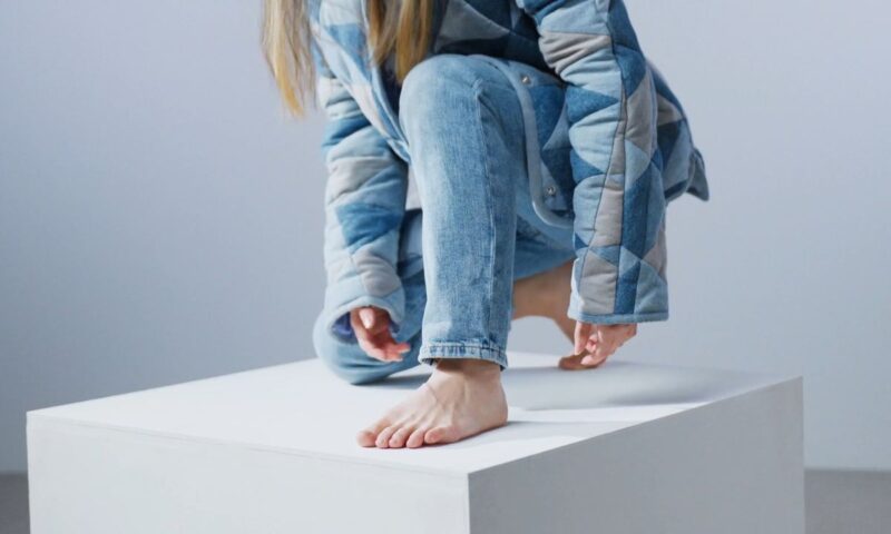 devojka u svetlo plavim farmerkama i svetlo plavoj jakni pozira bez obuće