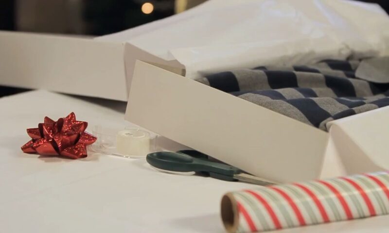 osoba pakuje majicu u kutiju i ukrašava ukrasnim papirom