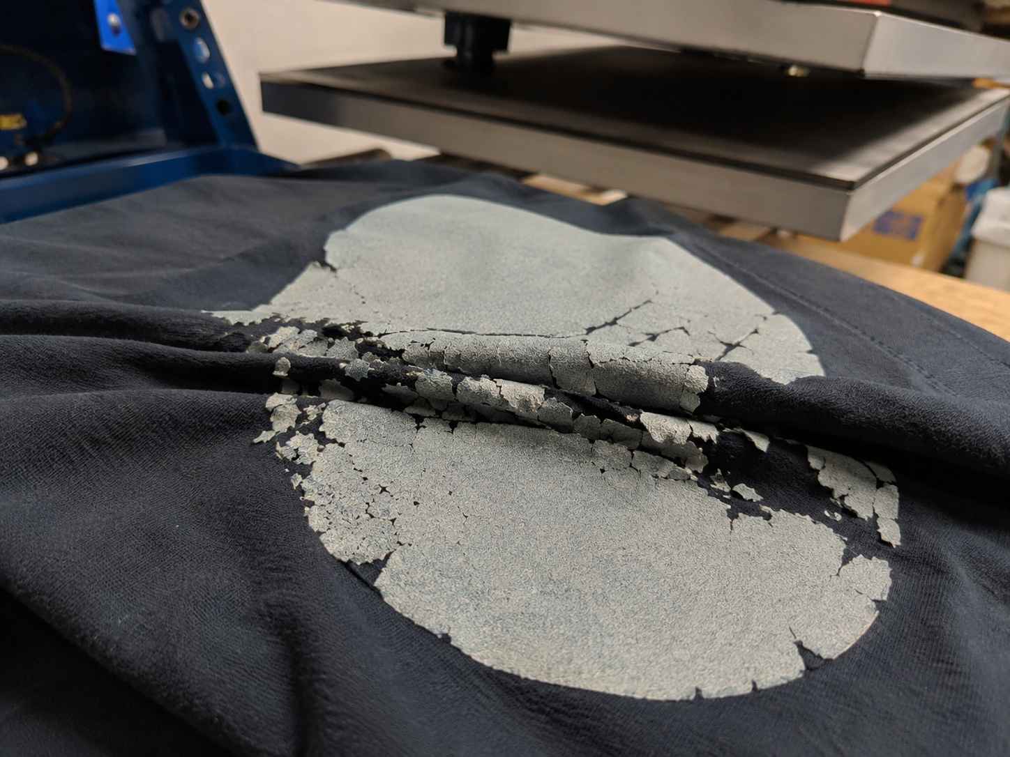 Napukla i oljuštena štampa na crnoj majici ispod prese za tekstil.